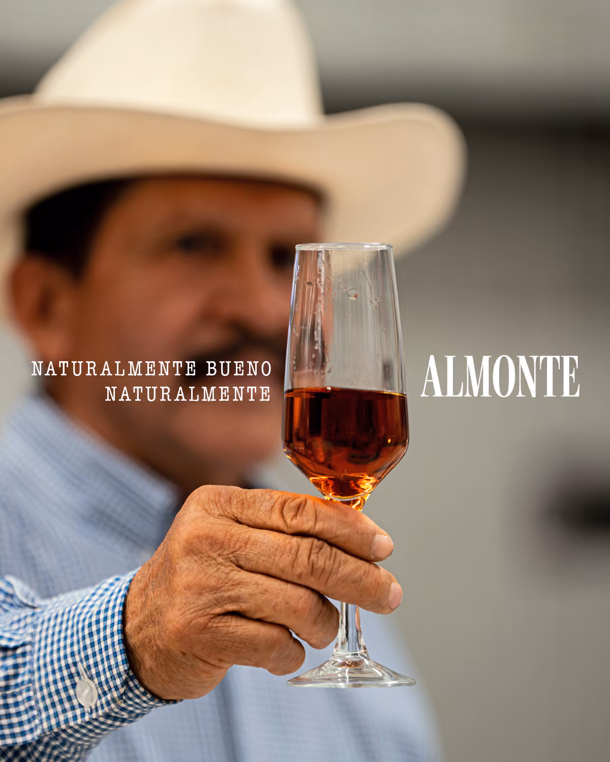 Hombre con sombrero que sostiene una copa de tequila frente a la cámara.