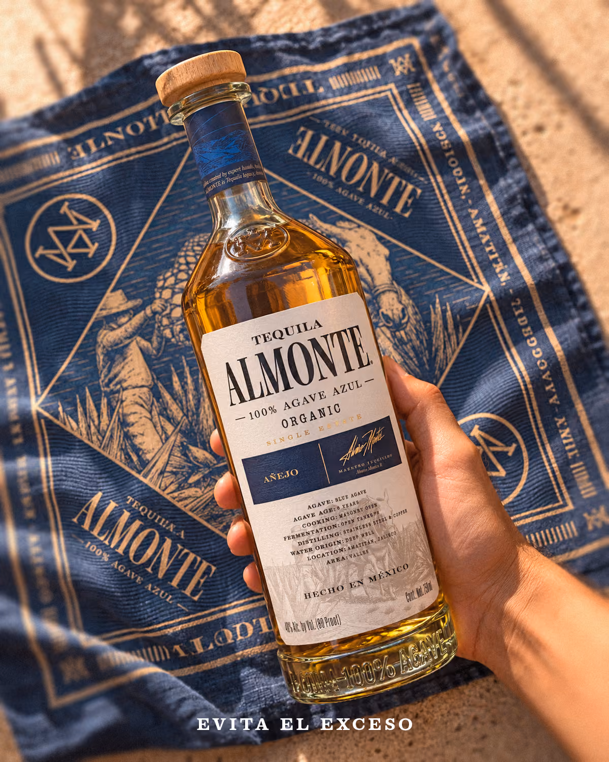 Botella de Almonte Añejo sostenida sobre un paliacate azul de la marca.